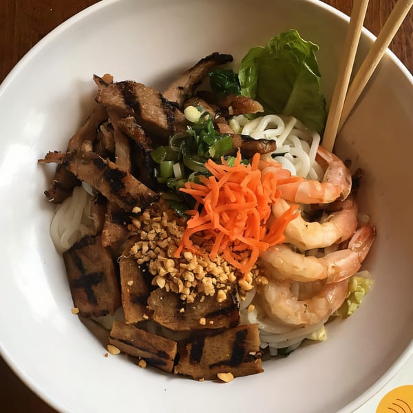 A Vietnamese vermicelli bowl with grilled pork, shrimp, noodles, carrots, peanuts, and lettuce.
