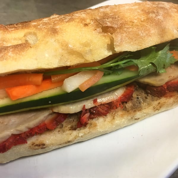 Close-up of a Vietnamese banh mi sandwich with pork, cilantro, carrots, and cucumber on a white plate.