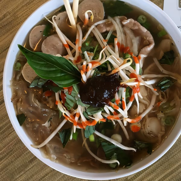 A bowl of Pho Yum's Vietnamese pho, topped with bean sprouts, basil, sriracha, and hoisin sauce.