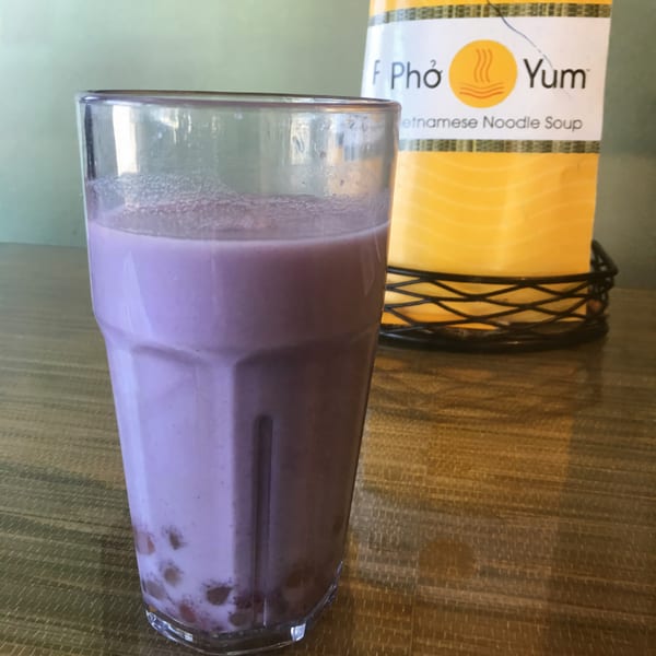 A glass of purple taro bubble tea with tapioca pearls, next to a Pho Yum menu.