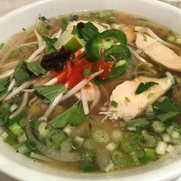 Close-up of Pho Yum's chicken pho with noodles, broth, herbs, lime, and chili sauce.