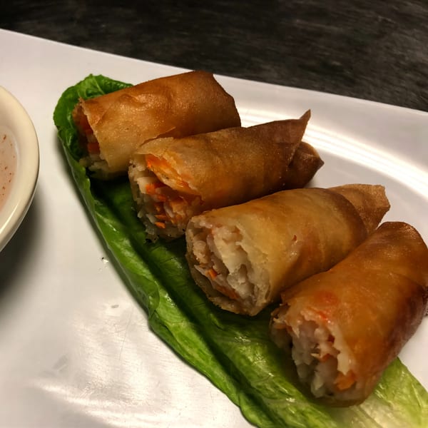 Four golden-brown Vietnamese spring rolls, filled with vegetables, served on a lettuce leaf with dipping sauce.