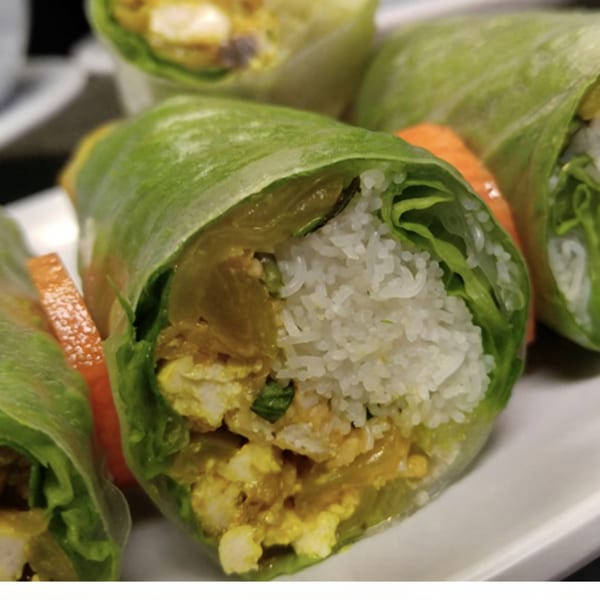 Close-up of Vietnamese spring rolls with rice, lettuce, and yellow filling on a white plate.